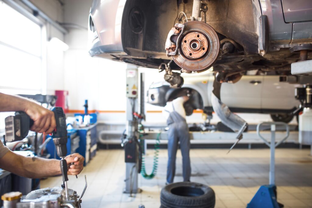 The car is lifted for repair on a lift in a car service station, a mechanic in overalls repairs